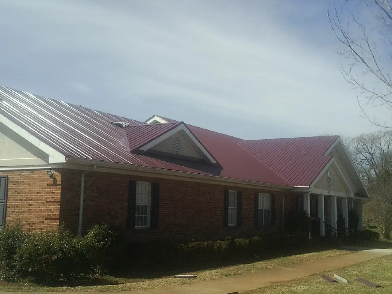 Red metal roof with gabled entries on a long brick building, from a Hail Damage Roof Repair job in Leeds
