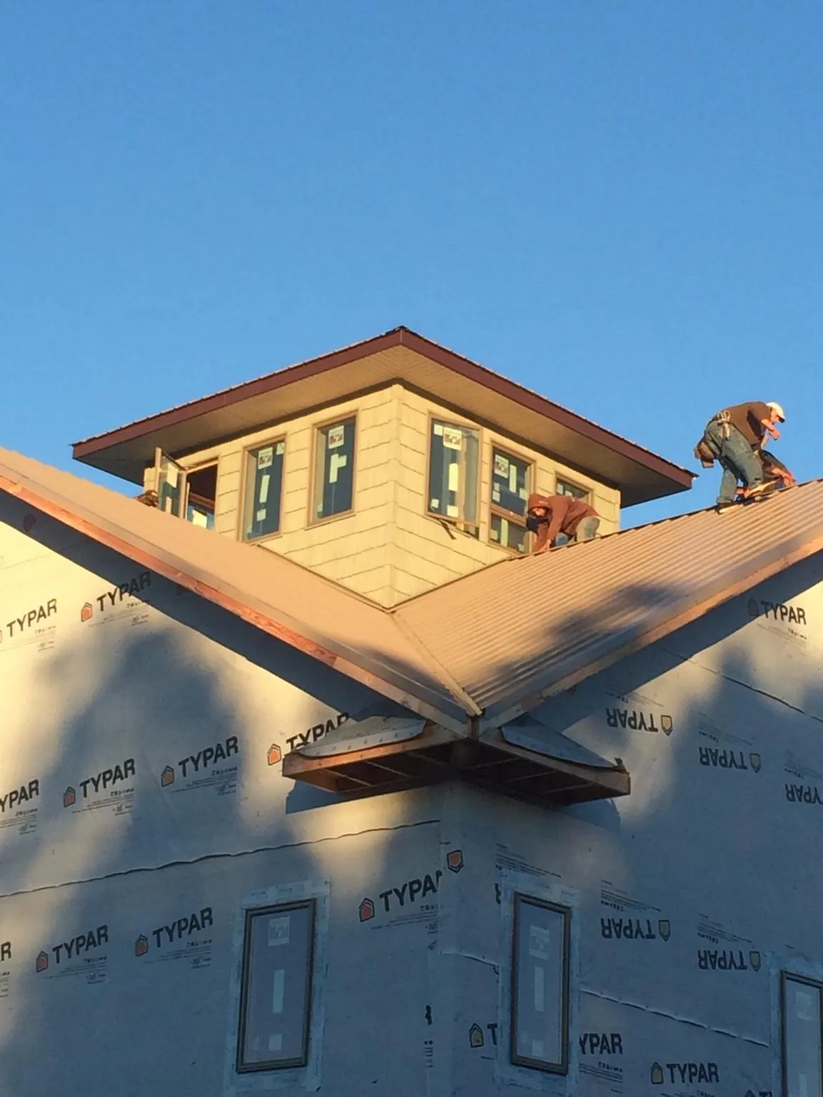 Roofers working around a rooftop cupola on a new metal roof at sunset — Roof Waterproofing in Leeds by Roofing Brothers